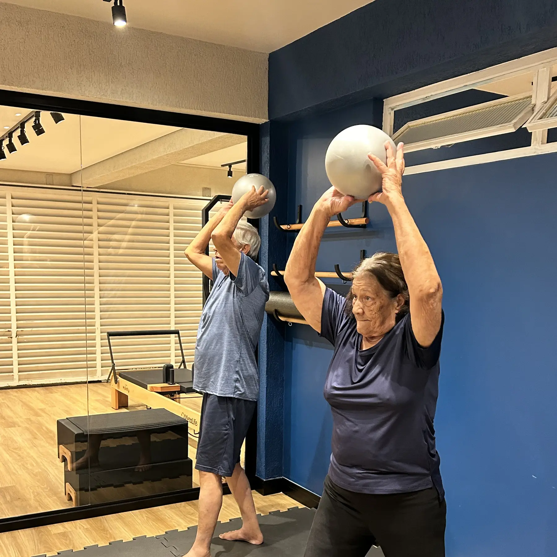 Aluna do Melo Franco Studio erguendo a bola suíça em frente à parede azul do studio