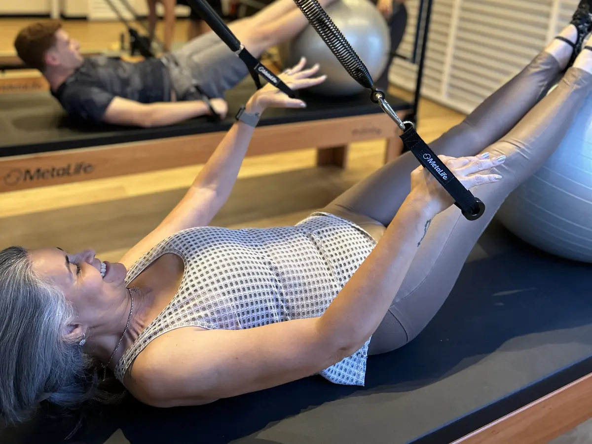 Aluna fazendo exercício com molas e bola suíça no aparelho, com outro aluno ao fundo